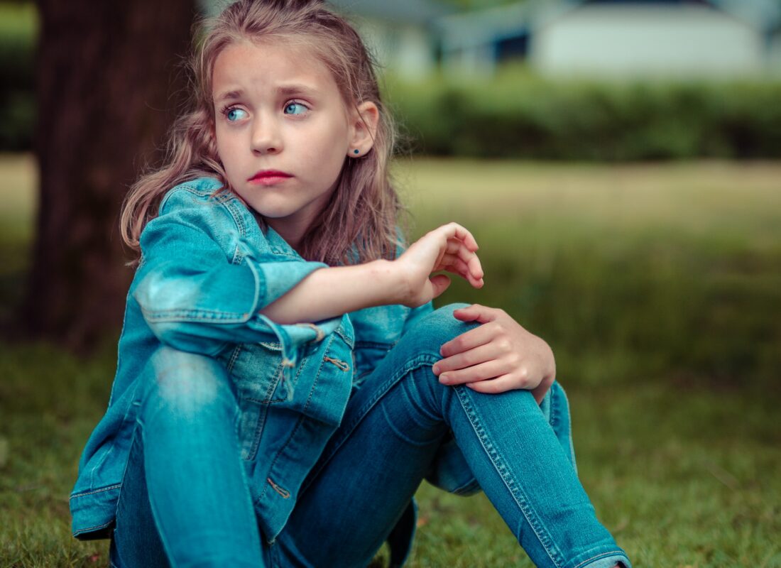 Girl sitting on the grass looking sad to illustrate parenting webinar by parenitng expert Anita Cleare on how too listen so children will talk