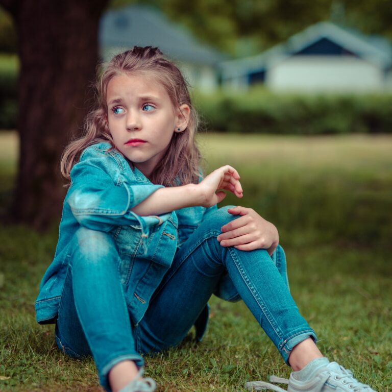 Girl sitting on the grass looking sad to illustrate parenting webinar by parenitng expert Anita Cleare on how too listen so children will talk
