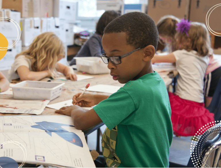 photo of young black boy wearing glasses in a classroom surrounded by children all working hard in exercise books, to illustrate article on school stress