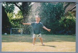 photo of young child standing in a garden sprinkler to illustrate a balanced childhood activity
