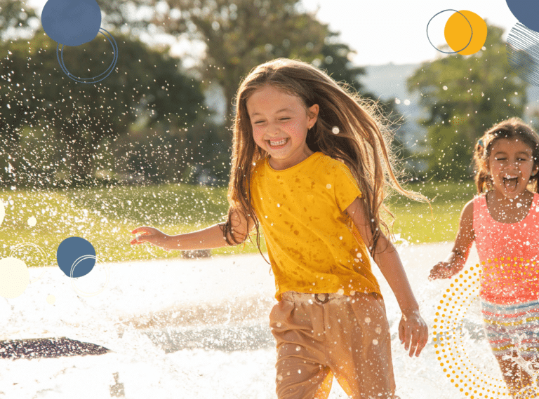 photo of two young girls running through a water sprinkler and smiling, to illustrate article on why positive parenting makes you happier