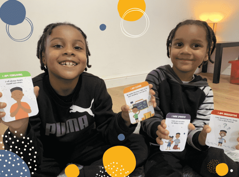 photo of two smiling boys holding positive affirmations cards to illustrate article on how positive affirmations can boost children's confidence