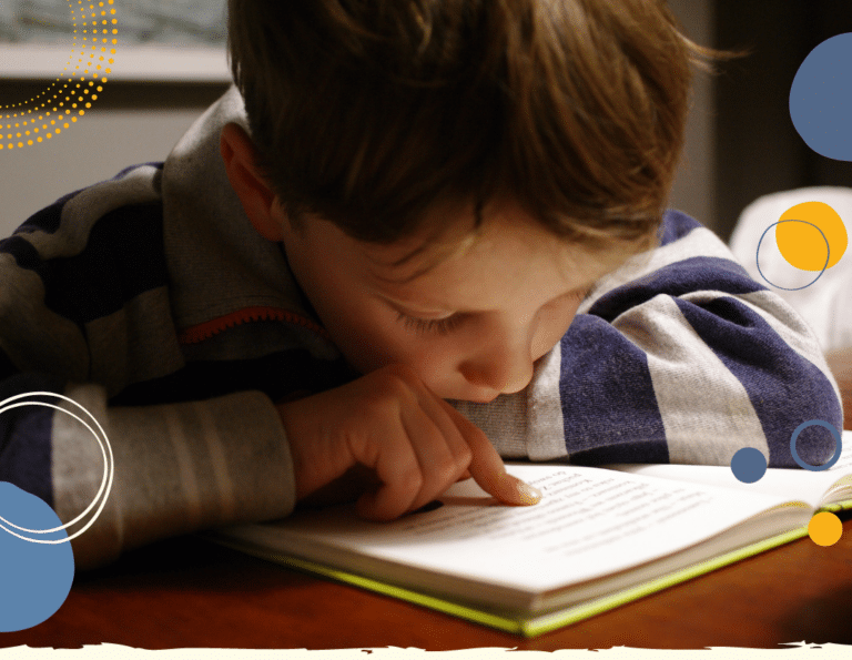 Close up photograph of 7-year-old boy reading a book intently, to illustrate article on How to encourage your child to read books