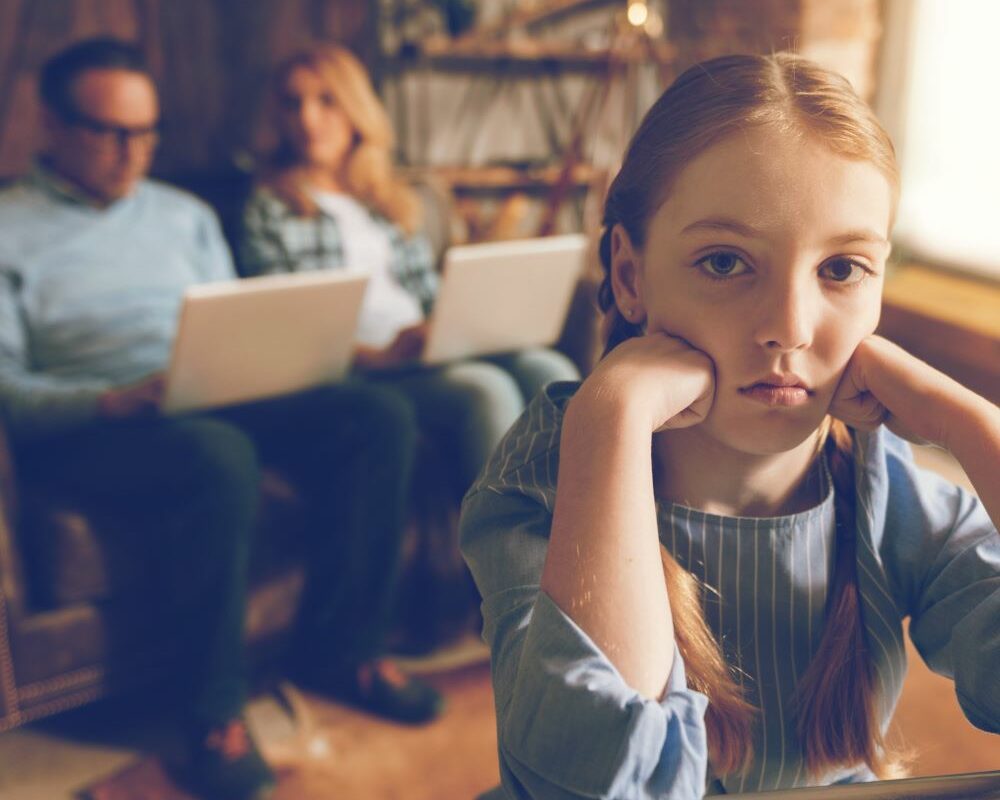 Photo of two parents on laptops ignoring bored child