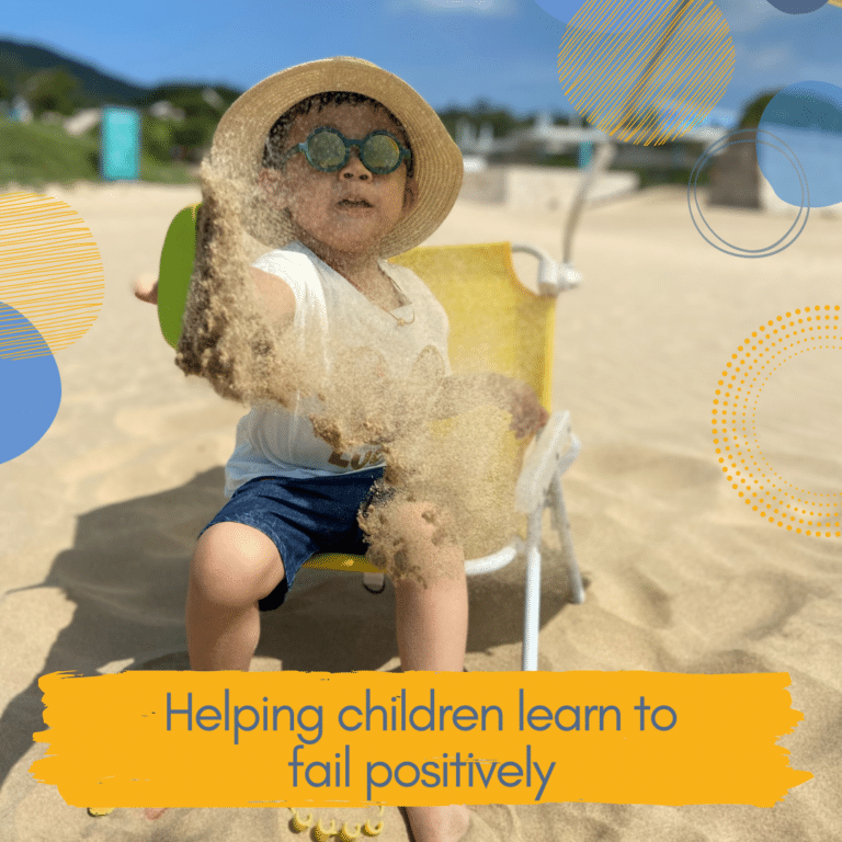 Young child wearing sunglasses and smiling on a beach with sand falling off their spade in the wind to illustrate article on helping children learn to fail positively