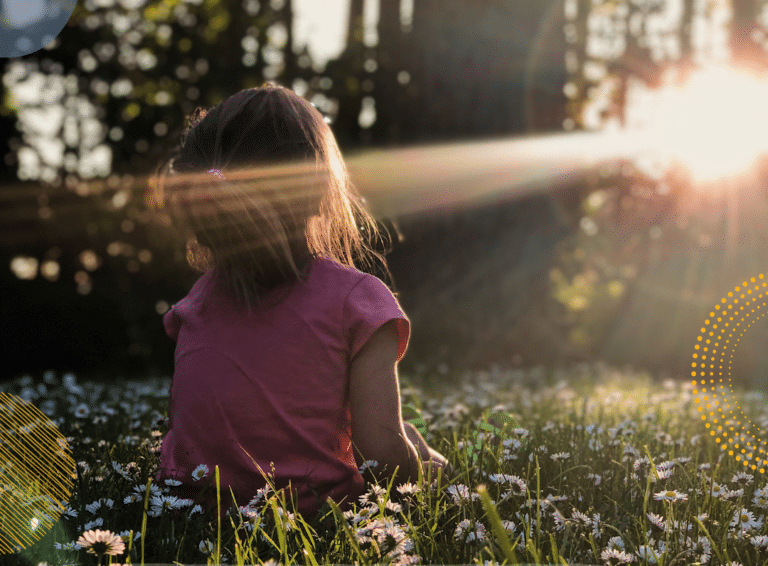 Photo of young girl sitting outside holding her face up to the sun streaming through the trees, to illustrate article on family mindfulness activities