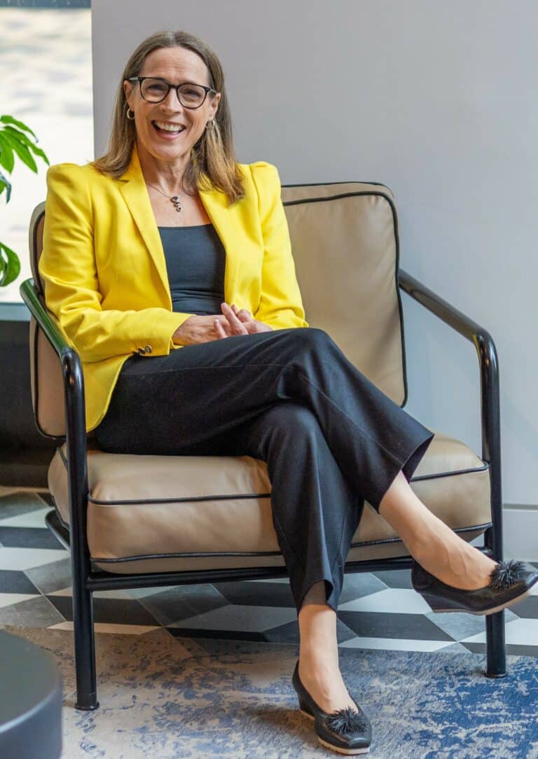 photo of parenting expert Anita Cleare wearing a yellow jacket, sitting in a brown leather chair smiling