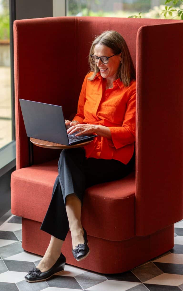 photo of parenting expert Anita Cleare wearing an orange blouse sitting in a work booth writing on a laptop