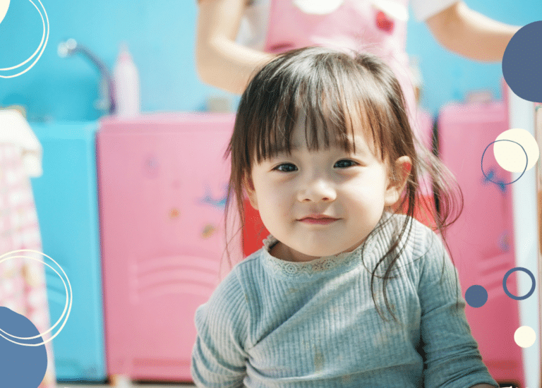 Photo of toddler smiling at the camera with adult standing behind