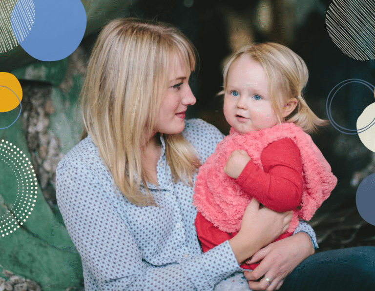 Photo of young white woman with blond hair holding a blond-haired toddler. The woman is looking at the toddler, the toddler is looking away. To illustrate article about parenting when you're autistic.